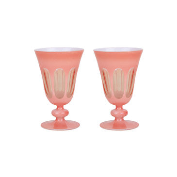 Pair of coral toned handblown curvy glasses. Short curvy stem with a round base topped with a tall curved cup with a mix of opaque and transparent ovals. White background.