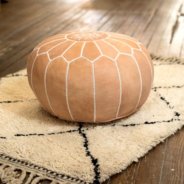 A Round Leather Pouf / Ottoman sitting on a Beni Ourain Rug. The pouf features classic Moroccan style embroidery up the sides and into the middle.
