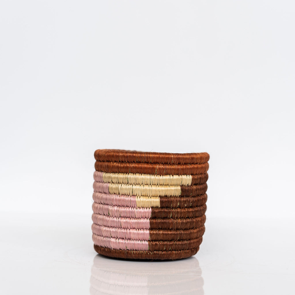 Handwoven Rwandan sweetgrass small straight sided basket in mahogany, burnt umber, cream, and pink. White background.