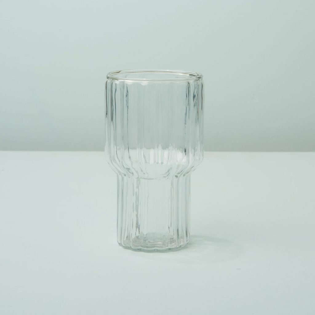 Ribbed texture handblown drinking glass that curves out at the halfway point. Sitting on an aqua background.