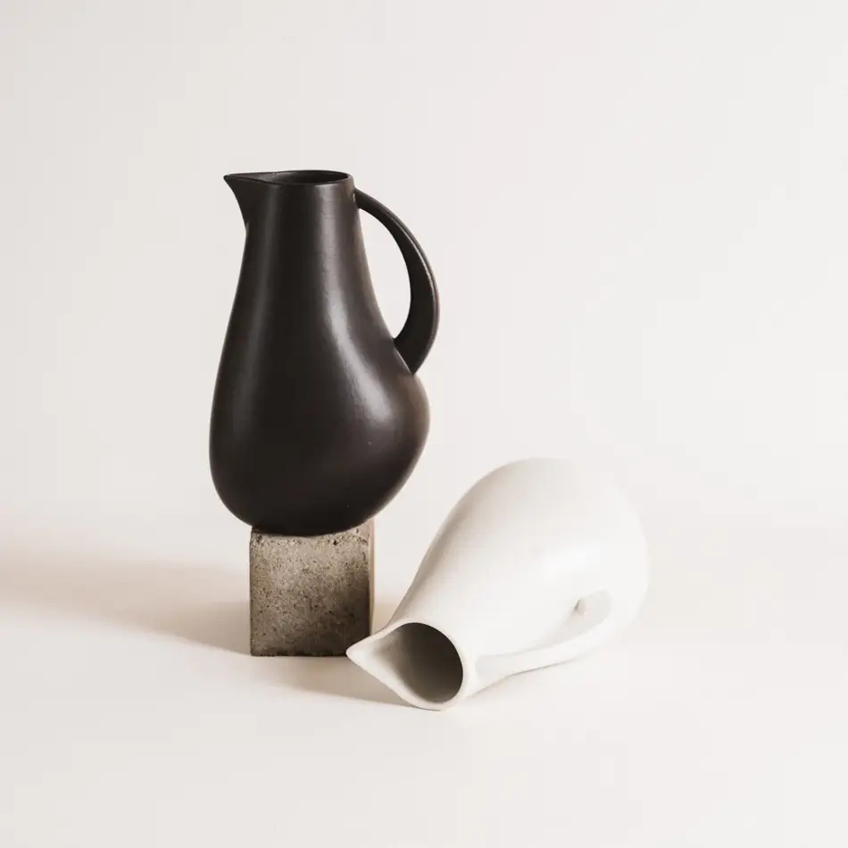 Two Stoneware pitchers, one black on top of a brick and one white laying on its side. White background.