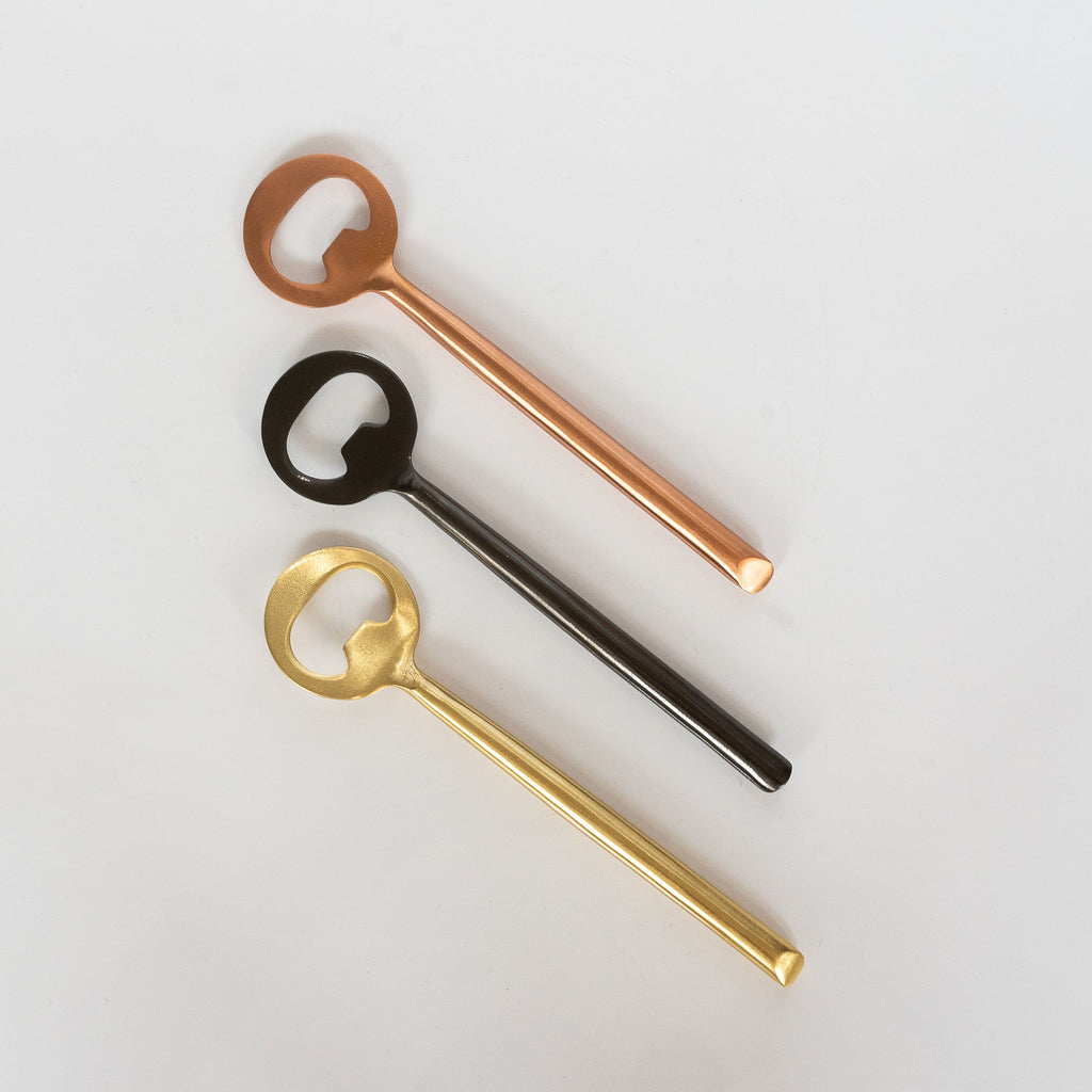 Three matte metal bottle openers, copper, matte black, and gold finishes. White background.