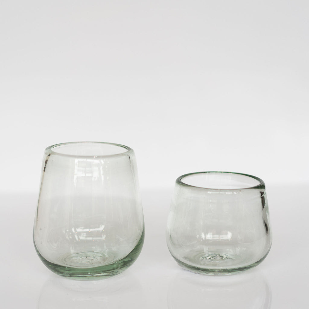 Two round elegantly curved clear handblown glasses sit on a light gray background.