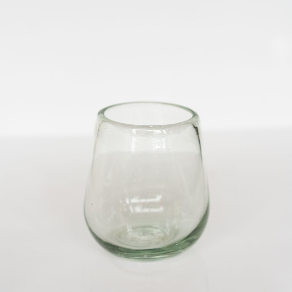 Elegantly curved clear handblown wine glass sits on a light gray background.