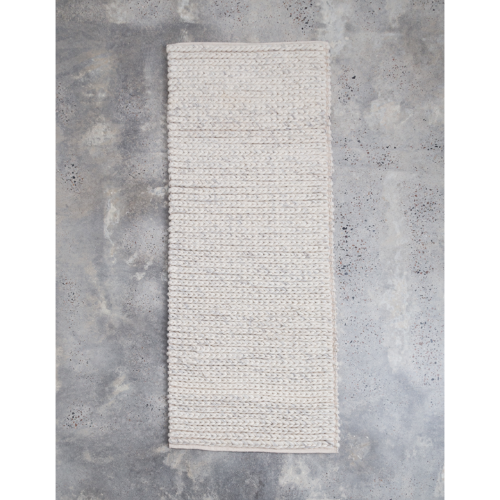 Braided natural toned wool knitted rug on gray background.