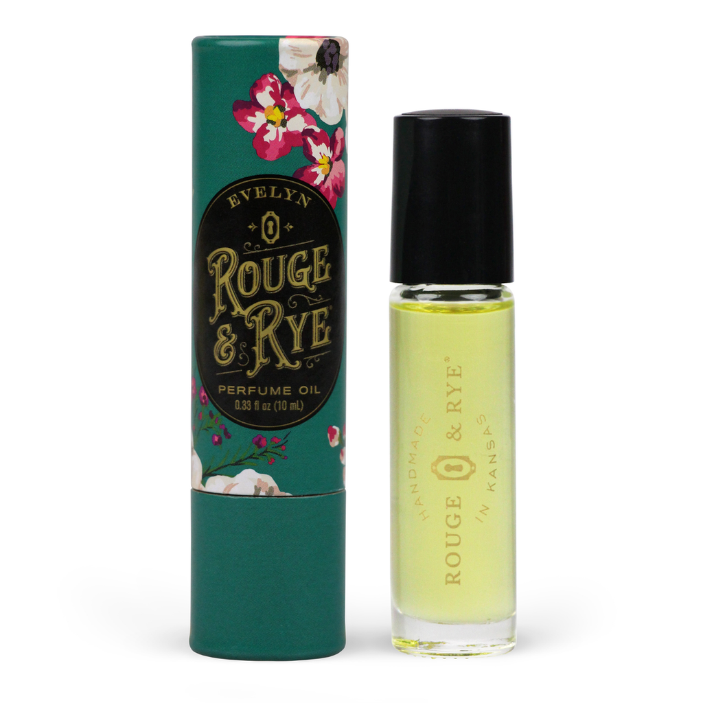 Golden Evelyn perfume oil roller in clear glass bottle with black plastic cap next to teal floral packaging. White background.