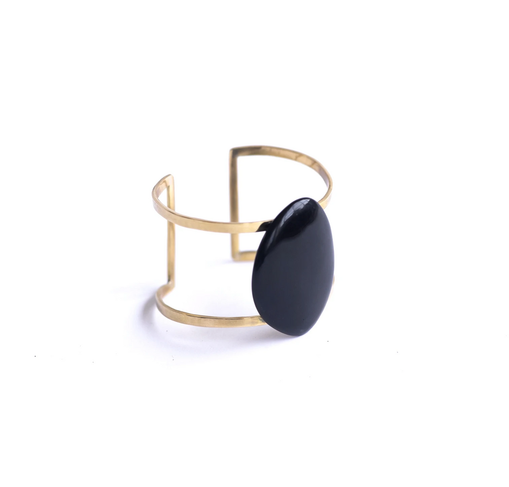 A brass adjustable cuff features a large oval ethically sourced black horn in the middle. Sits against a white background. 