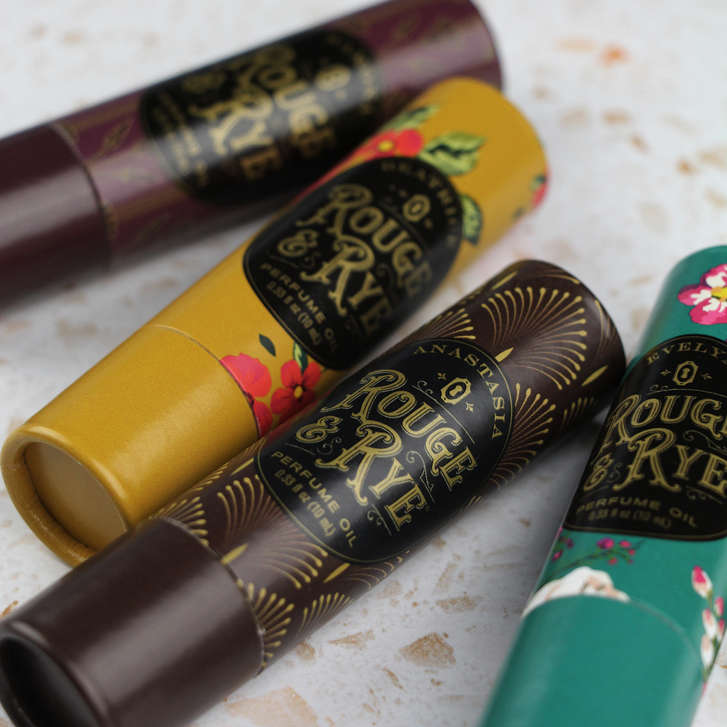 Four perfume roller oils in round cardboard packaging with art deco and floral designs. Terrazzo marble countertop.